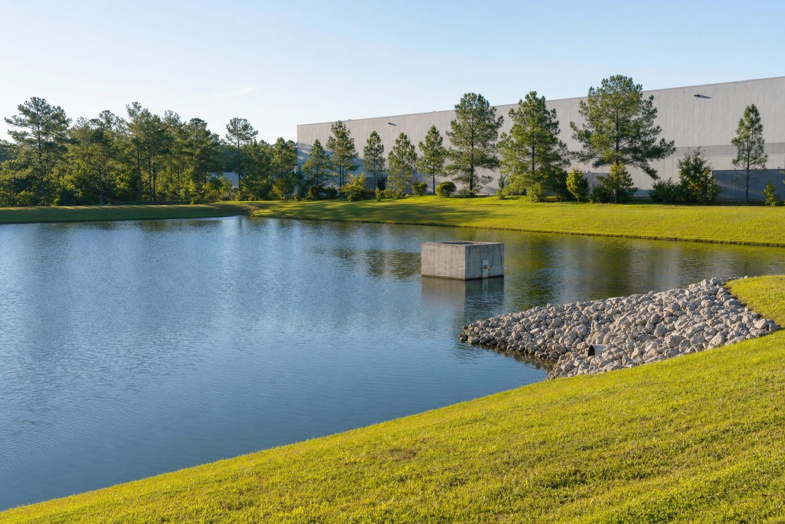 A clean stormwater catch pond with mowed banks and a concrete outfall structure at an industrial park